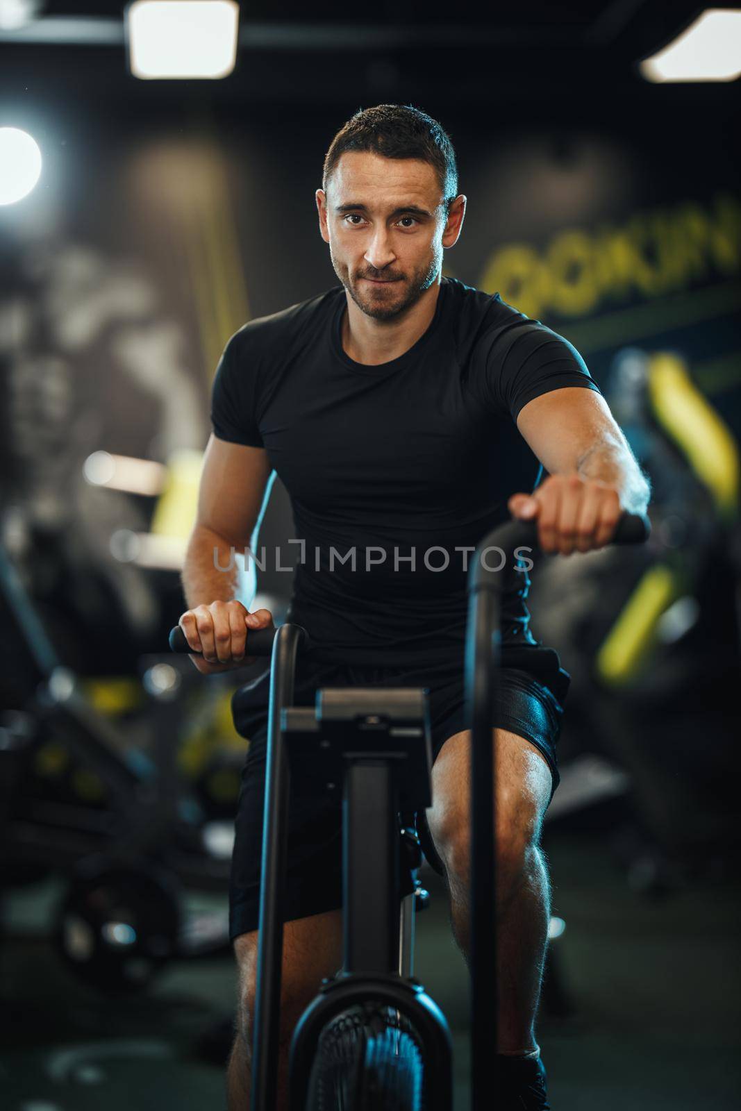 A young muscular man is doing hard cal bike crossfit training in the gym.