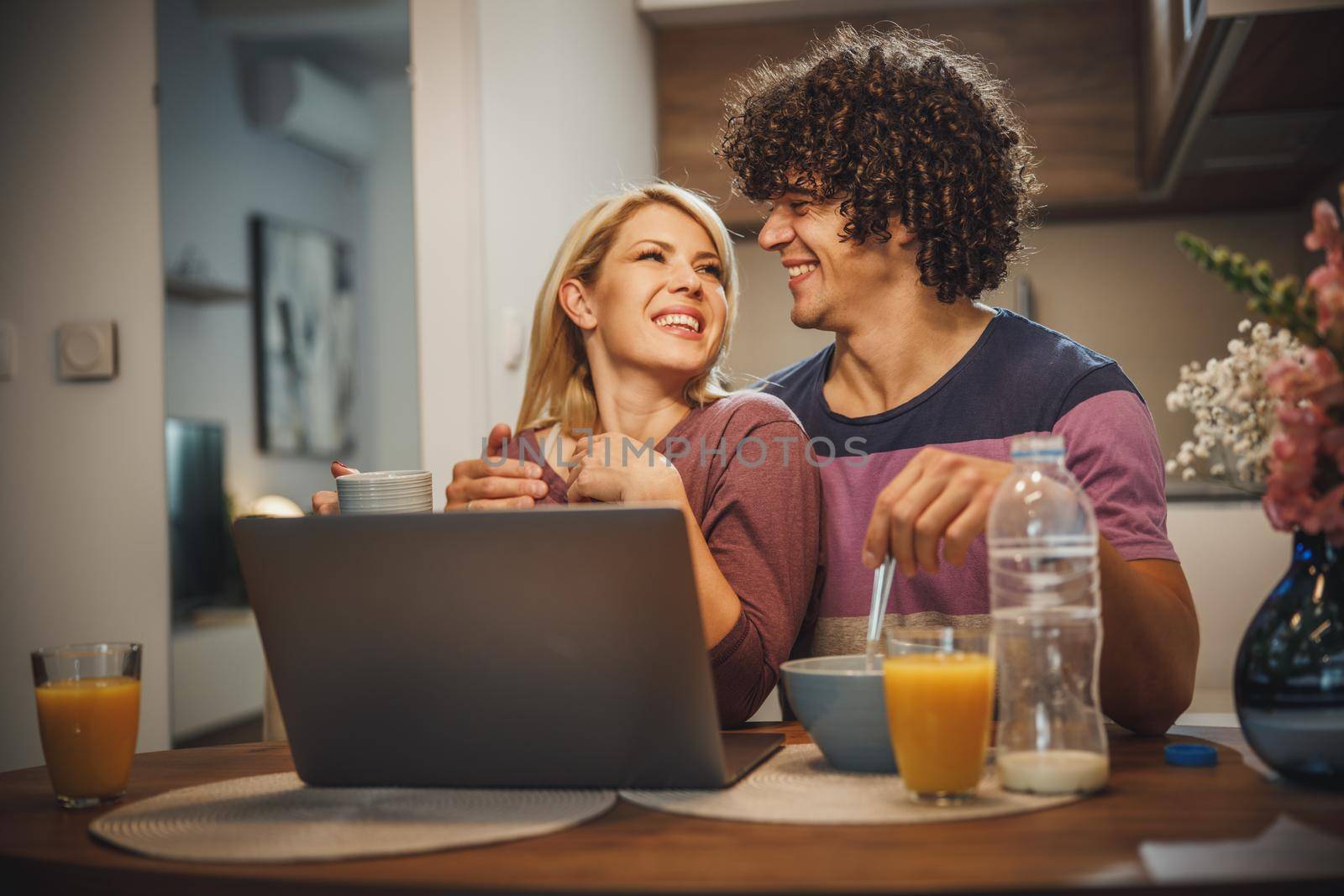 Shot of a happy couple using laptop together and eating breakfast before work in the kitchen.