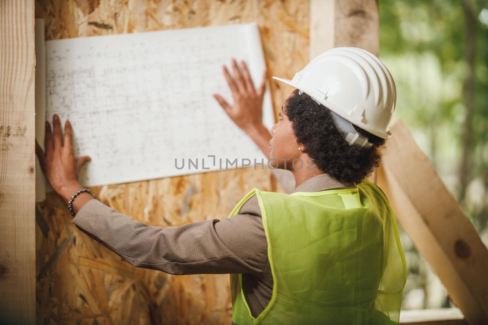 Shot of an African female architect checking construction site of a new wooden house. She is wearing protective workwear and white helmet.
