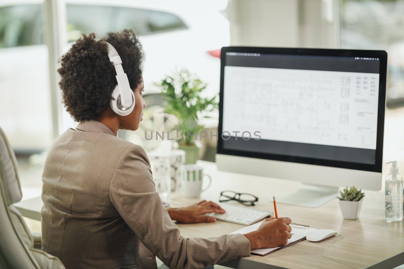 Shot of an attractive African businesswoman sitting alone in her home office with headphones and working on computer during COVID-19 pandemic.