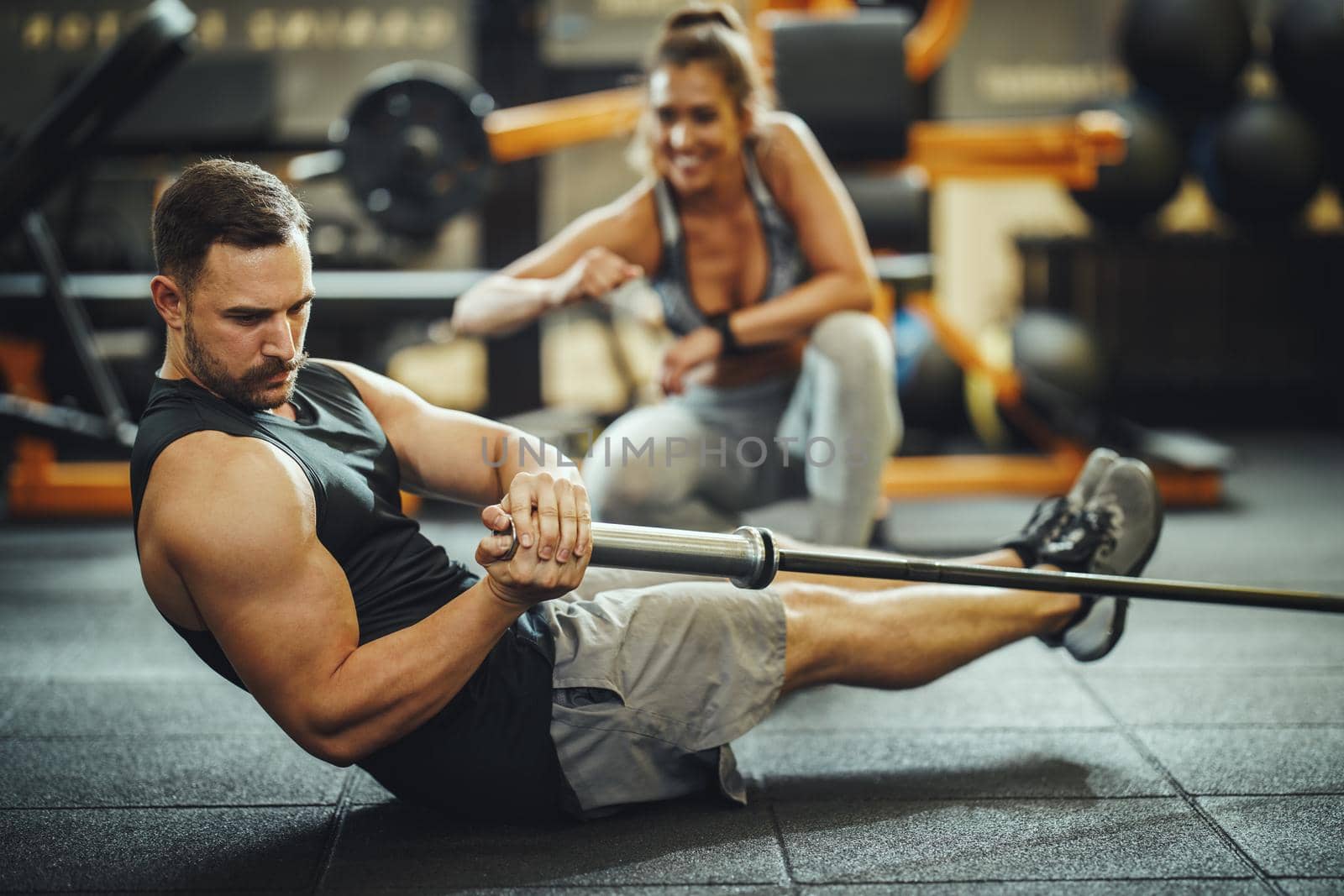 Shot of a muscular guy in sportswear working out with barbell at the cross training gym. He is pumping up abs muscule with heavy weight.