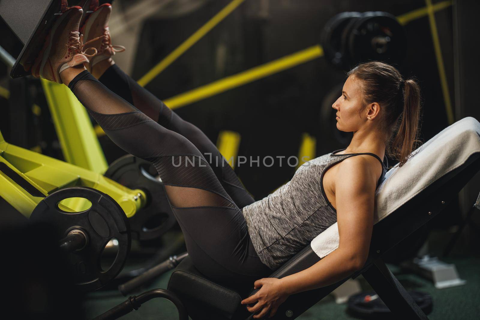 Shot of a muscular young woman in sportswear working out at the gym. She is doing exercises for her legs on leg press machine.