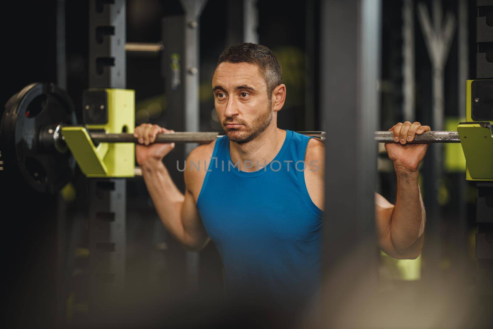 Shot of a muscular guy in sportswear working out at the cross training gym. He is doing squat exercises with barbell.