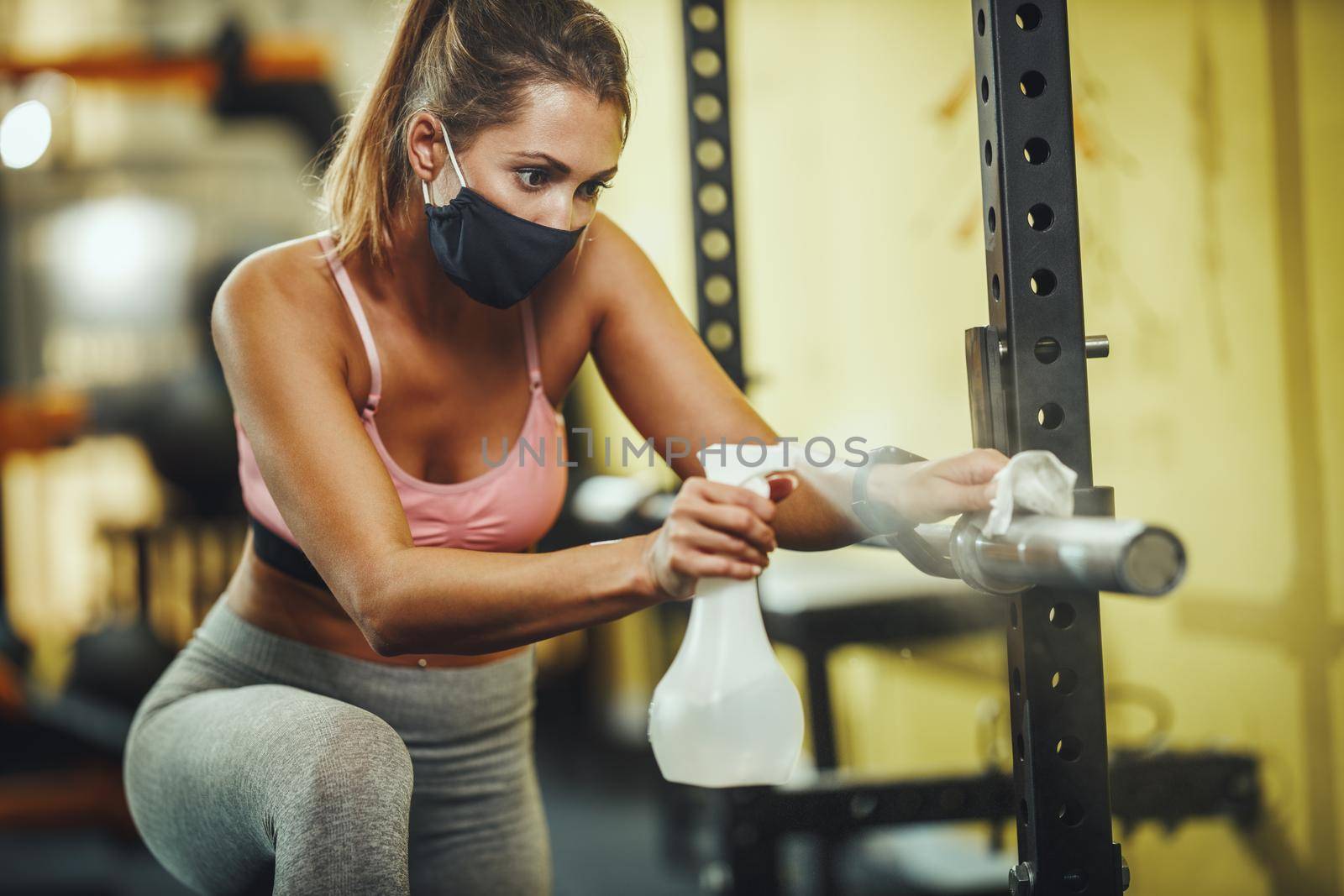 Shot of a muscular young woman with protective mask cleaning fitness gym equipment afther workout during Covid-19 pandemic.