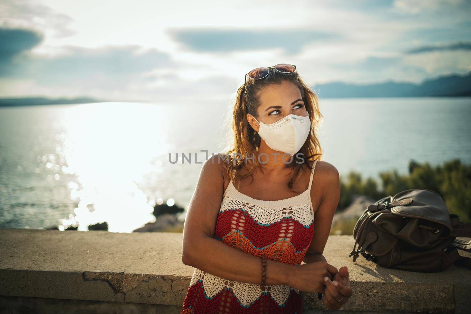 Shot of a happy young woman with protective mask spending time on seaside during exploring a Mediterranean at corona pandemic. 