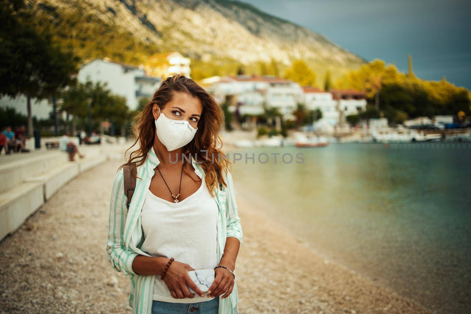 Shot of a pensive young woman with protective N95 mask while walking on the beach during the COVID-19.