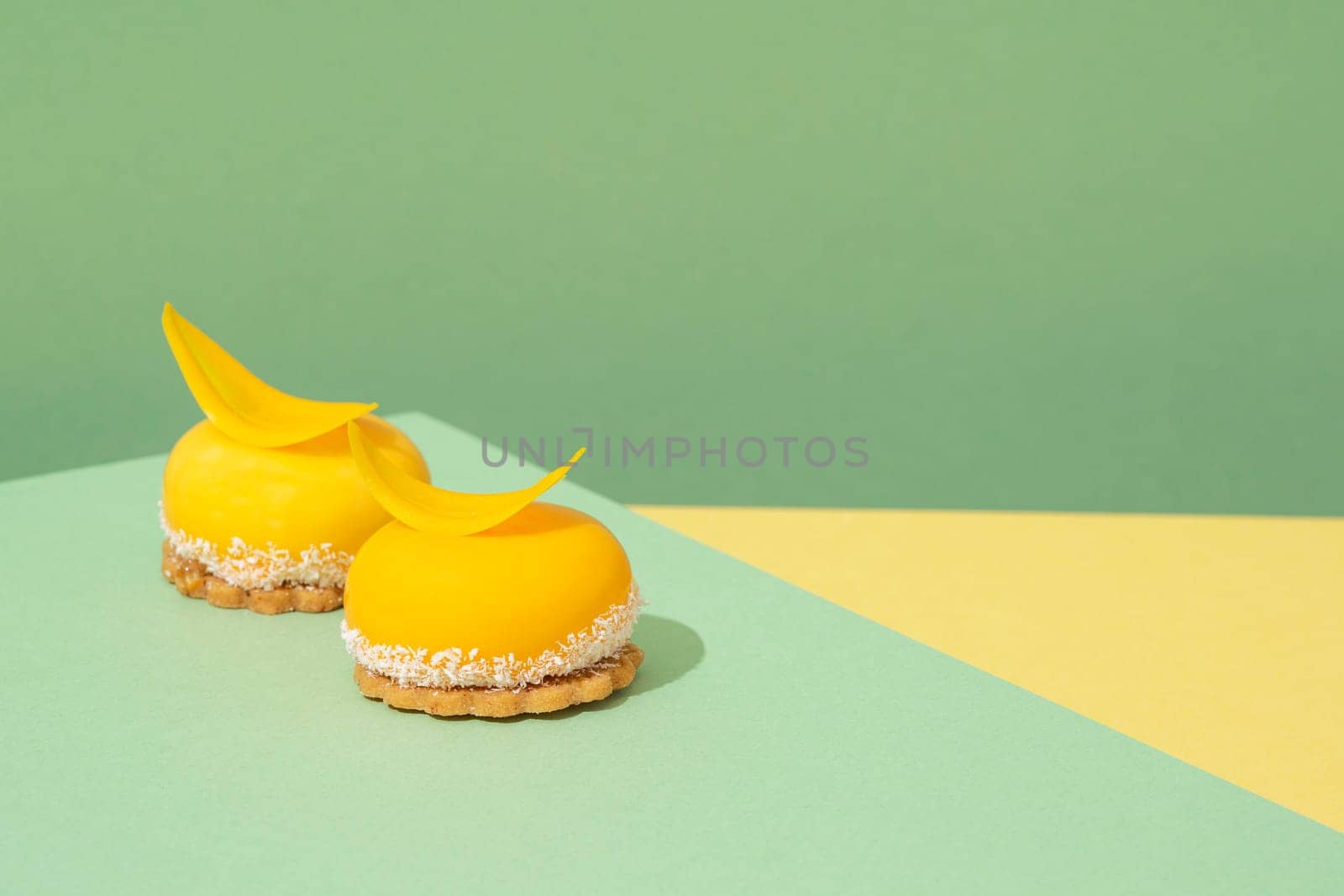 Two miniature, yellow-colored sweet treats set atop a blue and yellow-patterned tabletop by A_Karim
