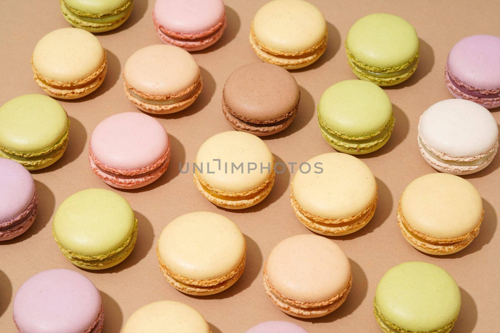 An overhead shot of a beige table surface featuring an array of colorful macarons in neat rows by A_Karim