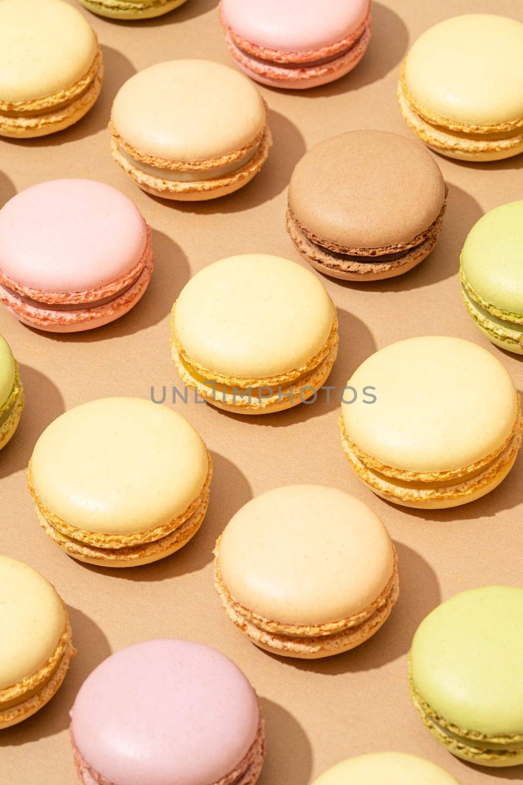 An overhead shot of a beige table surface featuring an array of colorful macarons in neat rows by A_Karim