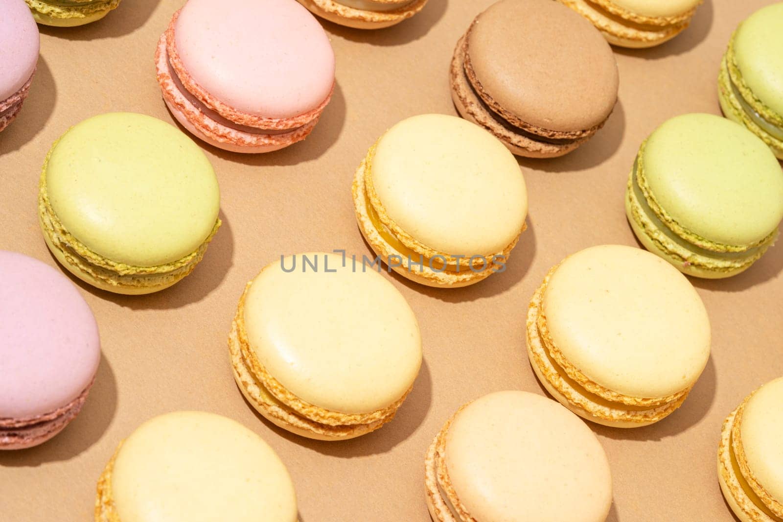 An overhead shot of a beige table surface featuring an array of colorful macarons in neat rows by A_Karim