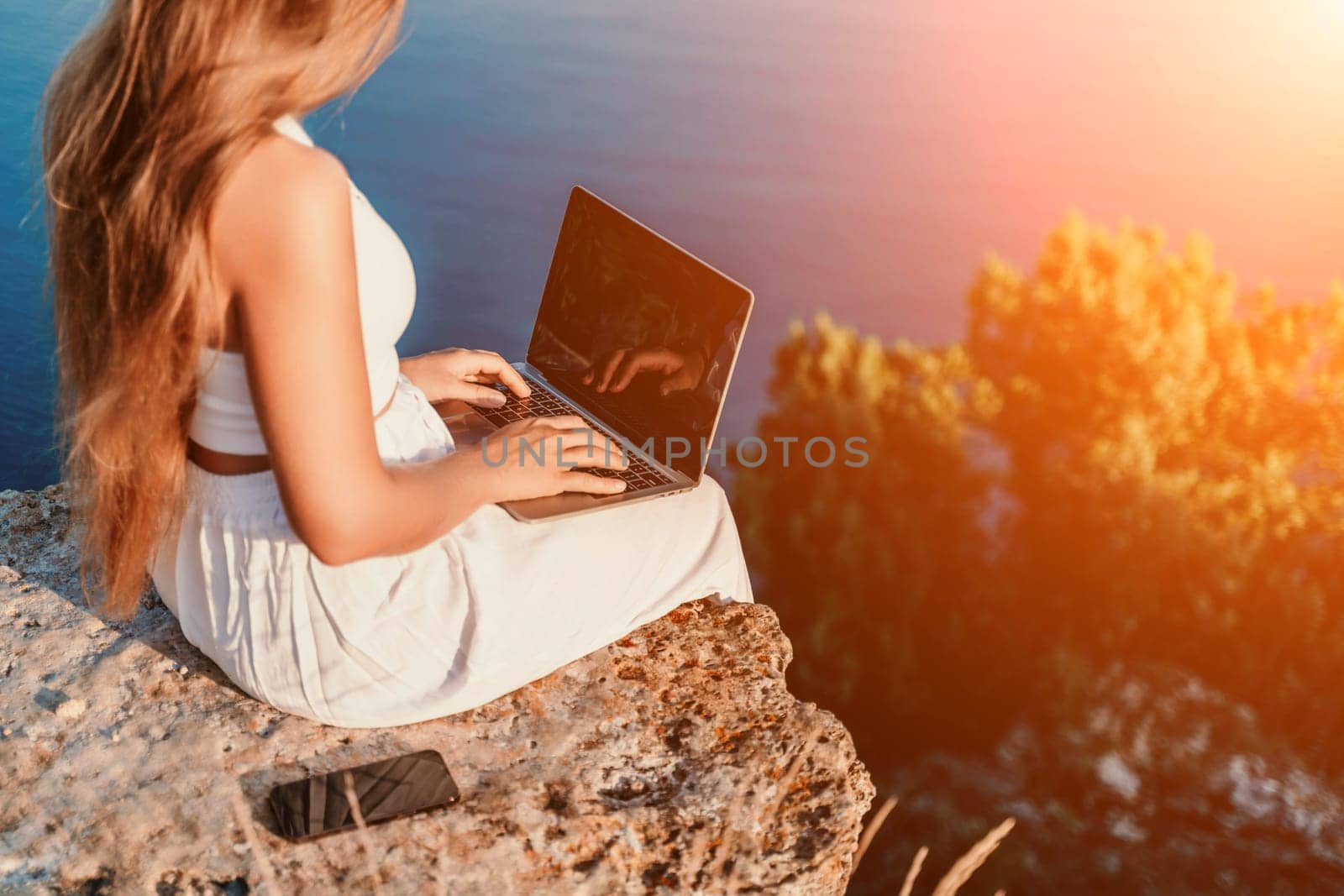 Freelance happy woman typing on her laptop, enjoying the picturesque sea view, highlighting the idea of working remotely with a relaxed and pleasant atmosphere