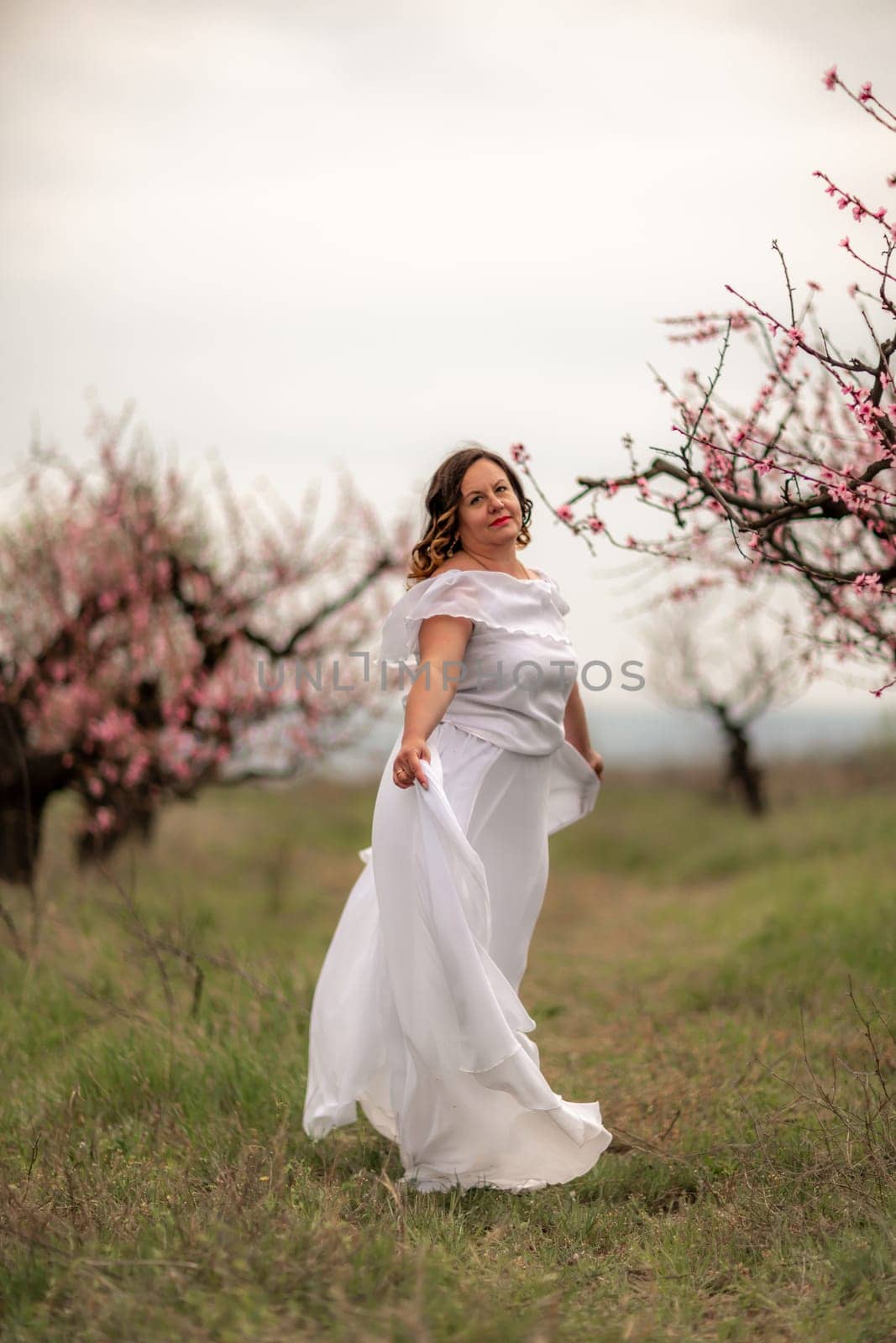 Woman peach blossom. Happy woman in white dress walking in the garden of blossoming peach trees in spring.