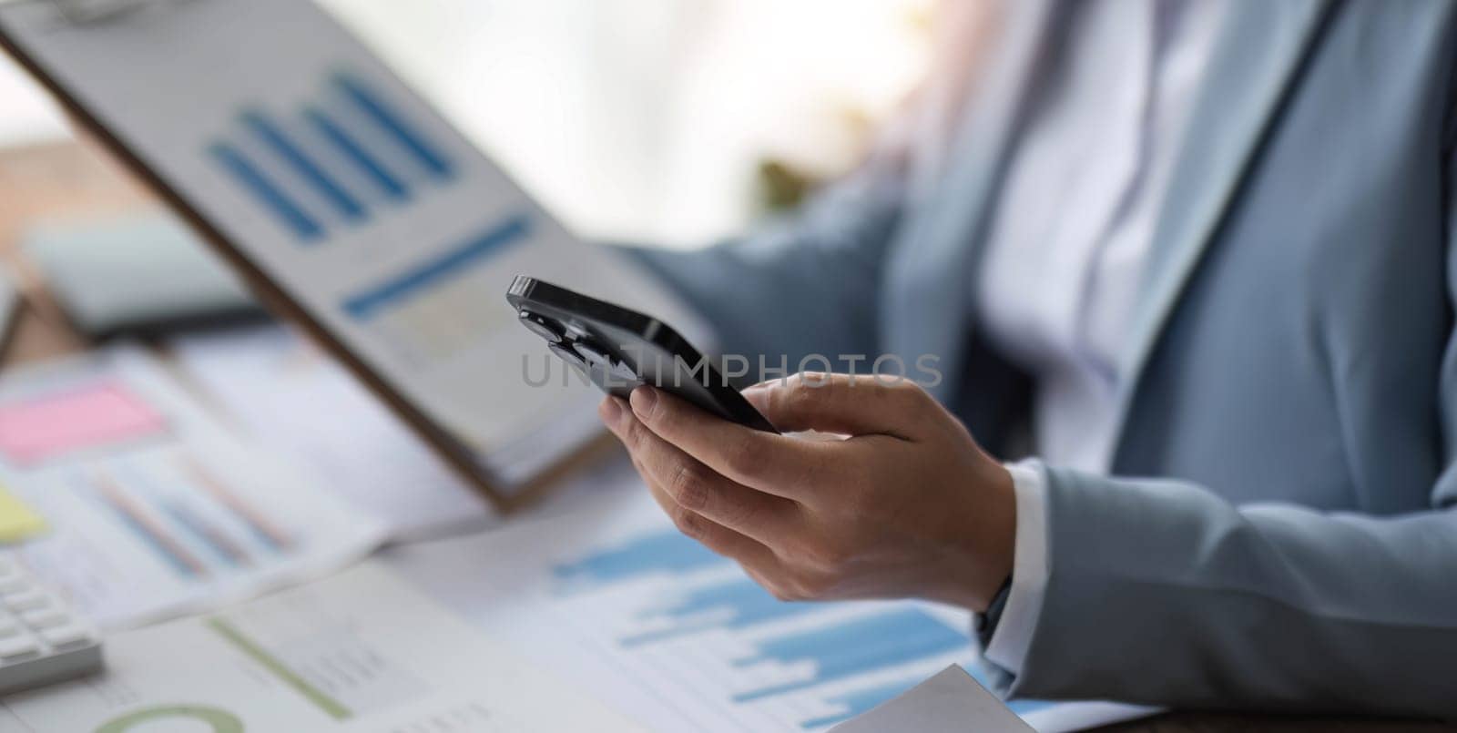 Close up businesswoman holding report using mobile phone and laptop computer on office desk, Business communication concept.