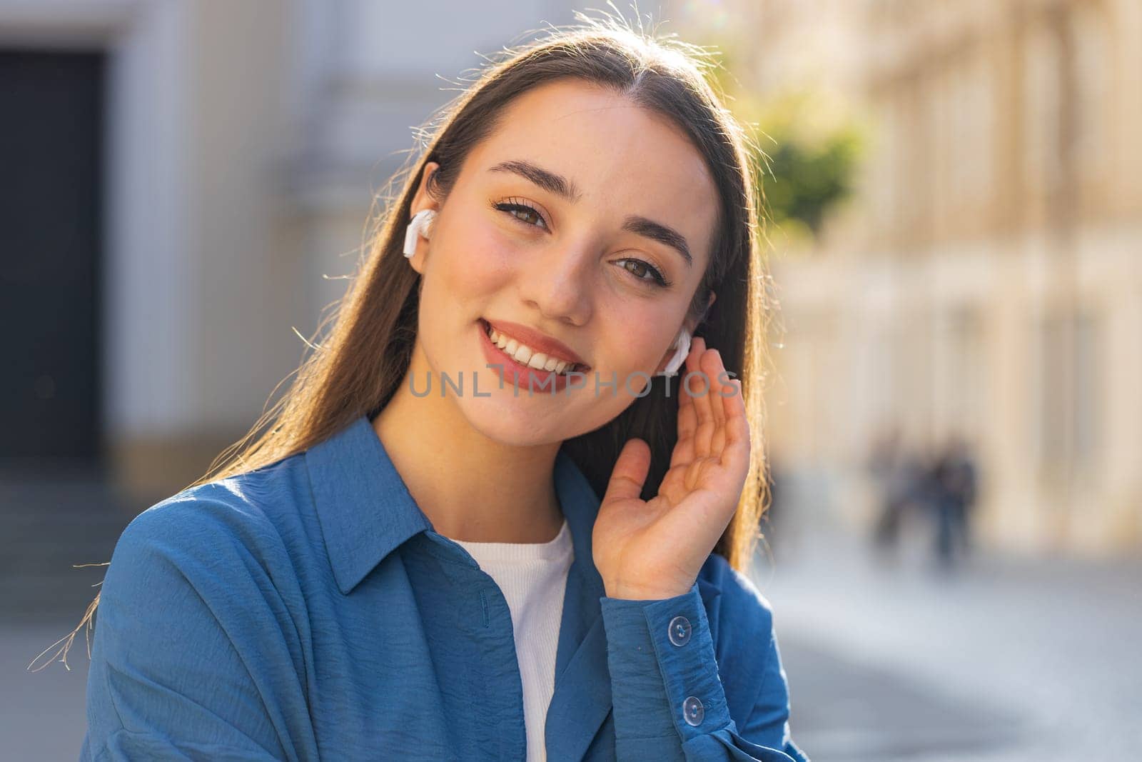 Happy relaxed overjoyed young pretty woman in wireless earphones choosing listening favorite energetic disco rock n roll music dancing looking at camera outdoors. Tourist girl walking in city street