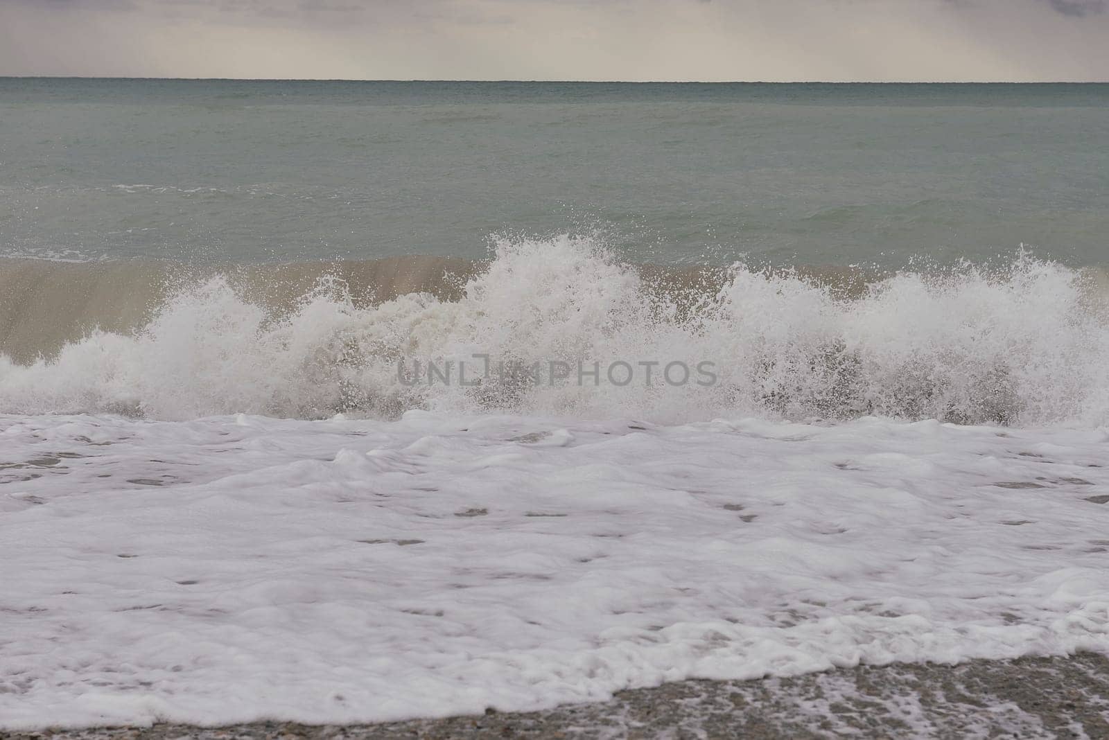Waves breaking on the shore on small pebble beach. Storm clouds sky, turquoise water, waves,