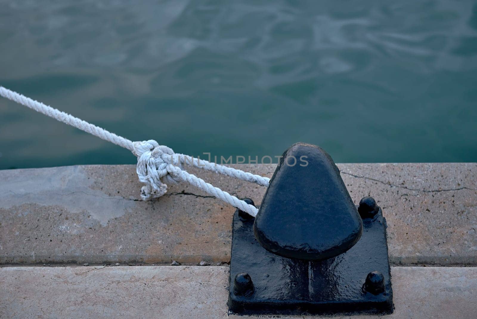 A bollard with a white rope tied to it from a harbour. detail, lineas, solitario, cuerda blanca, colour metallic, mar transparent