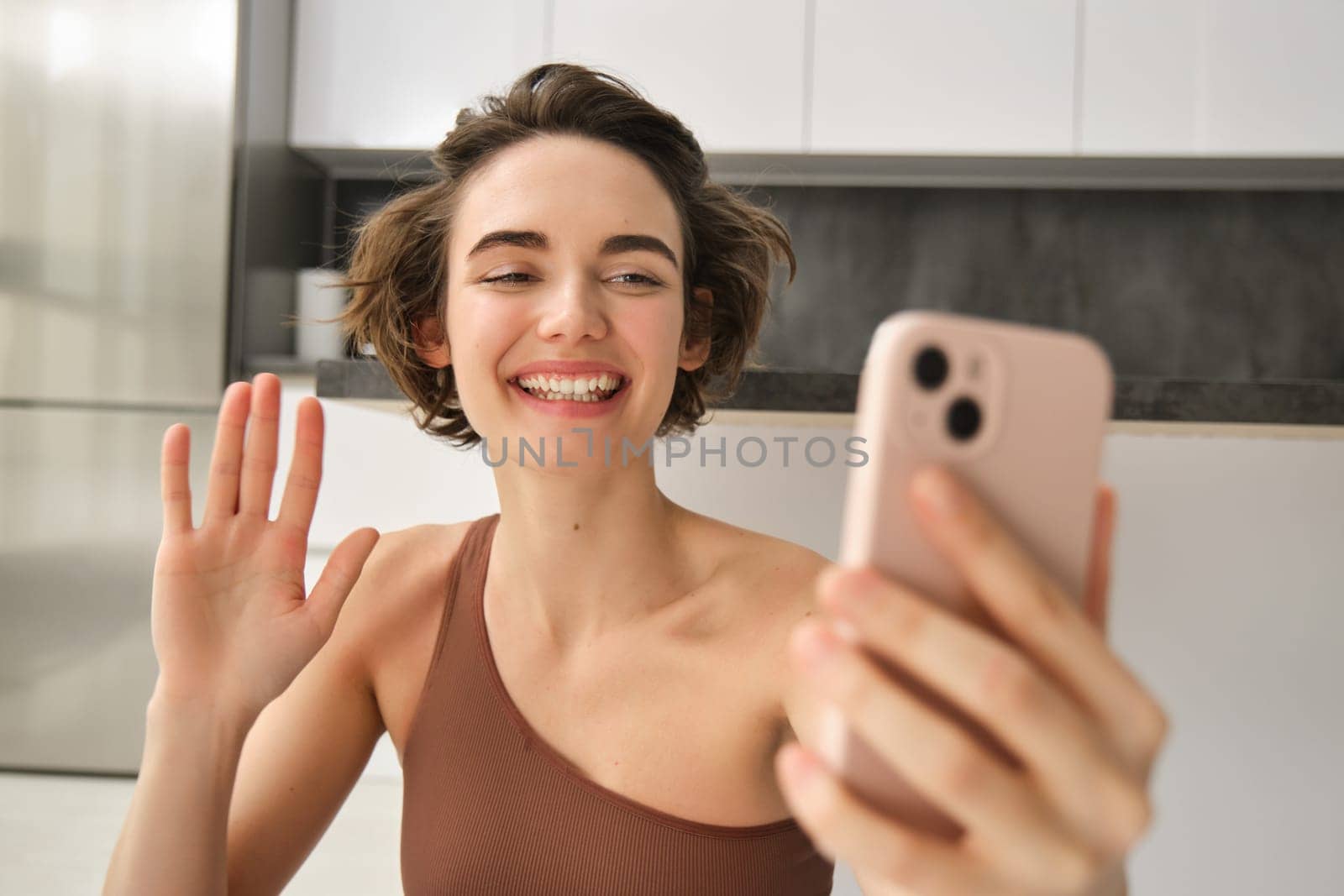 Portrait of young fitness woman, sitting at home on rubber mat, records video on smartphone, doing workout vlog, making live online training session from home. Copy space