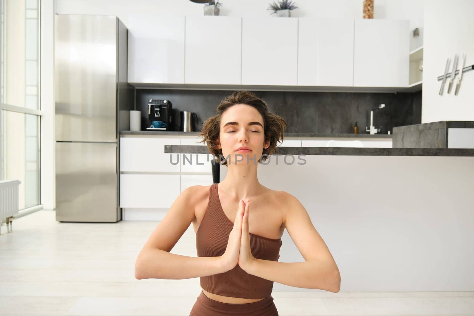 Beautiful cute sporty woman doing exercise in bright room. Focused brunette sitting on the floor practicing yoga wear top and leggings. Home mood, lifestyle.