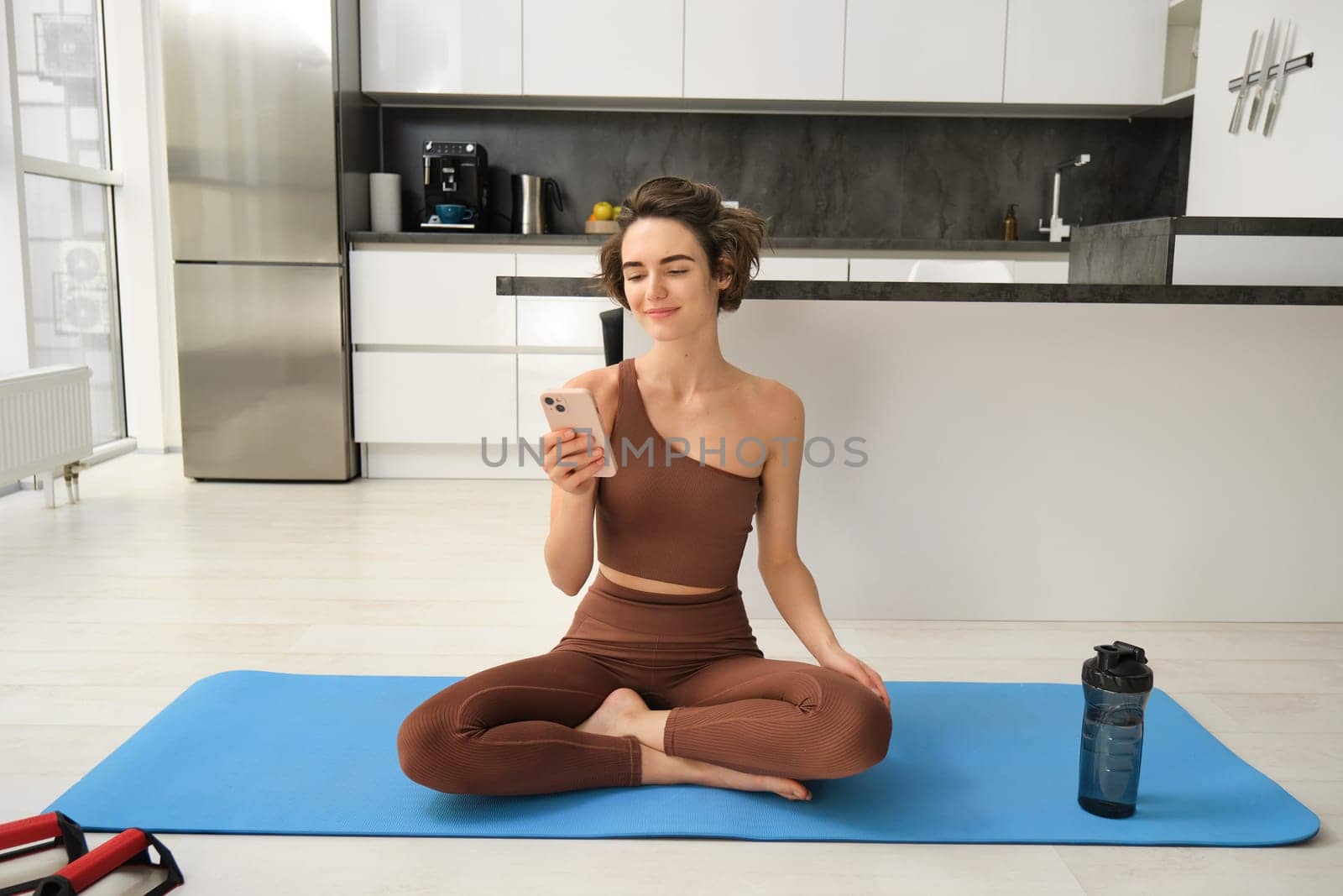 Portrait of young girl athelte, sportswoman sits at home, watching yoga, fitness video tutorials, workout alone indoors on rubber mat. Sport and lifestyle concept