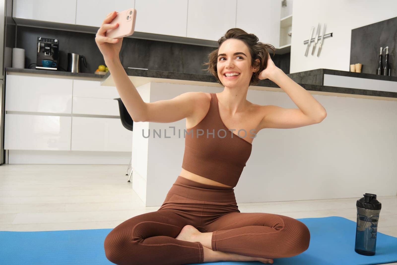 Lifestyle and workout. Modern fitness girl takes selfie on yoga mat, does her exercises at home and makes photos on smartphone, records live vlog, video on phone.