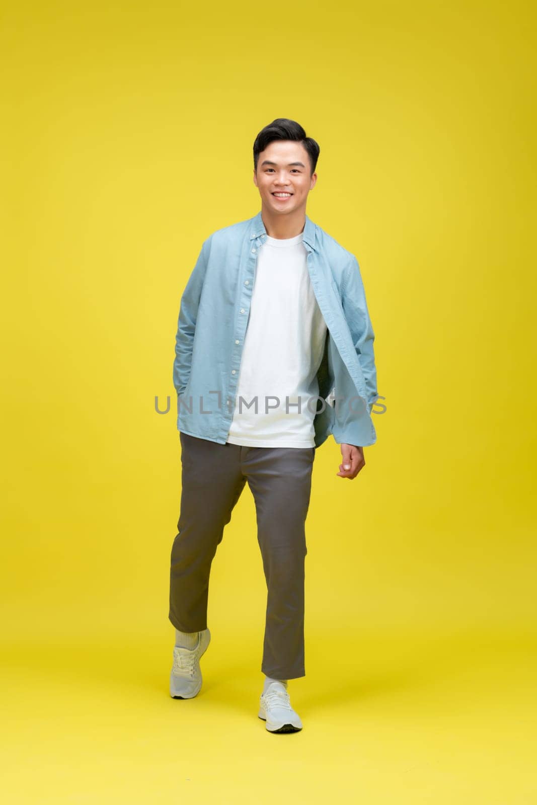 young asian man go walk step look empty space isolated over yellow background by makidotvn