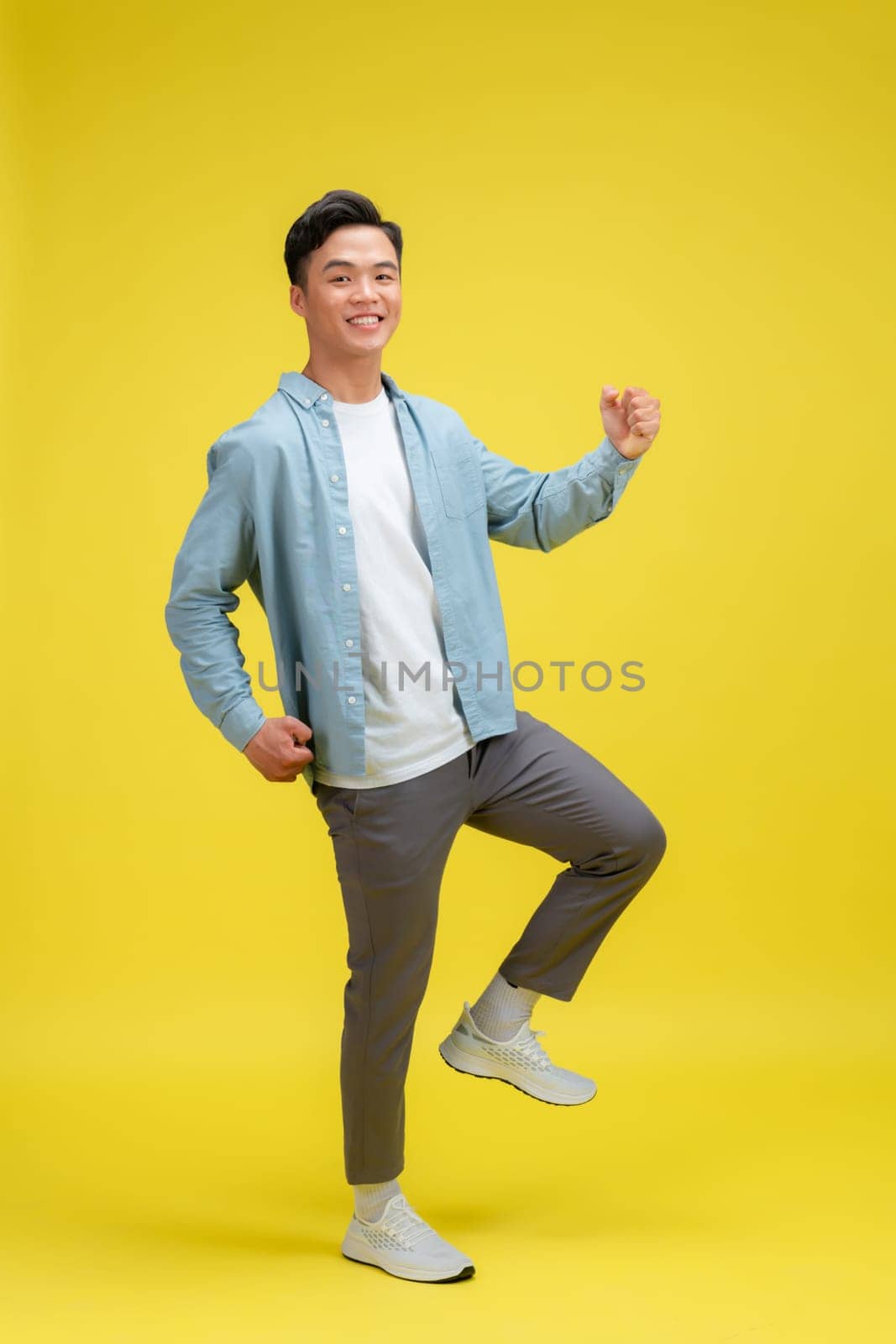 Young handsome man standing over isolated yellow background very happy and excited doing winner gesture with arms raised