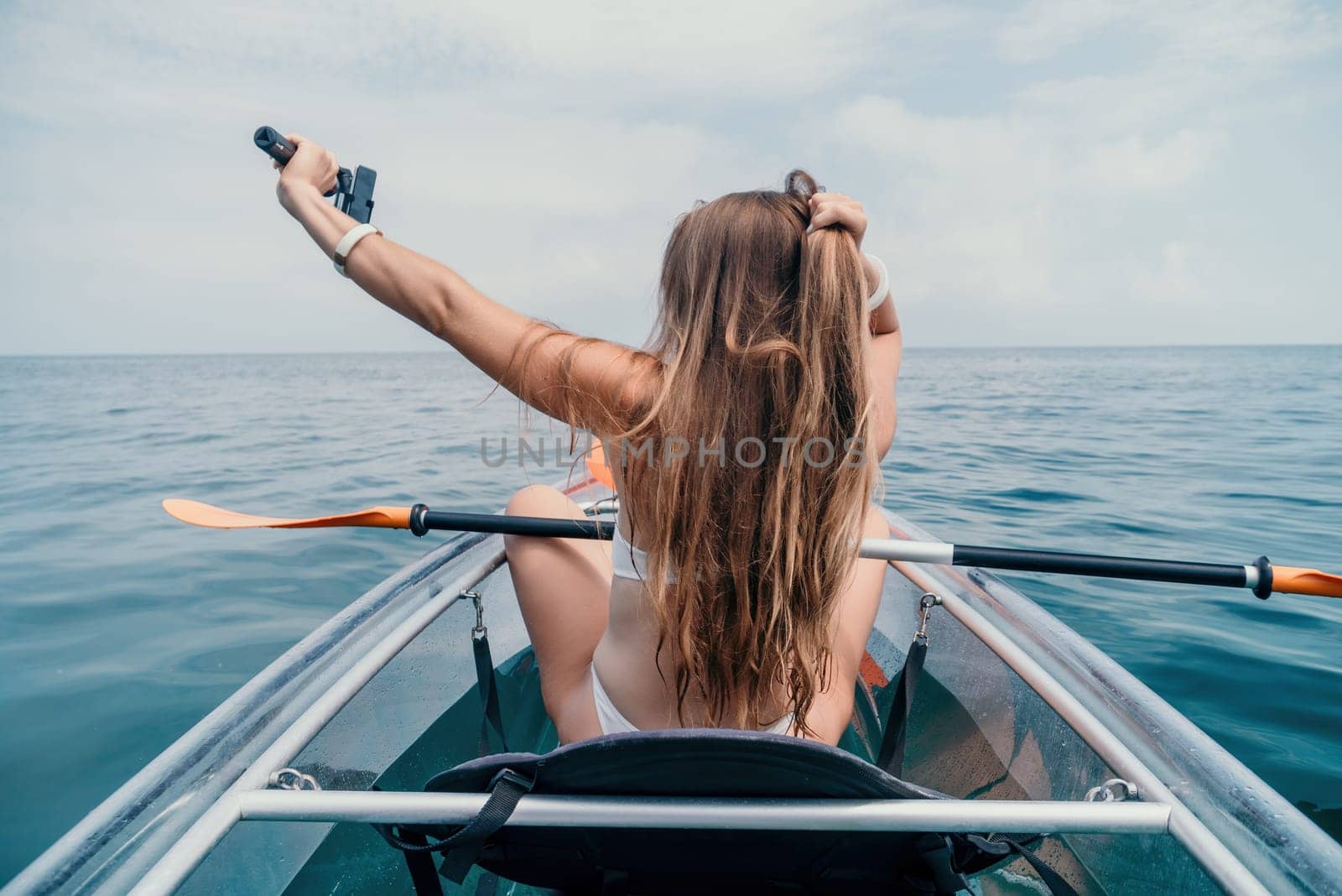 Woman in kayak back view. Happy young woman with long hair floating in transparent kayak on the crystal clear sea. Summer holiday vacation and cheerful female people relaxing having fun on the boat by panophotograph