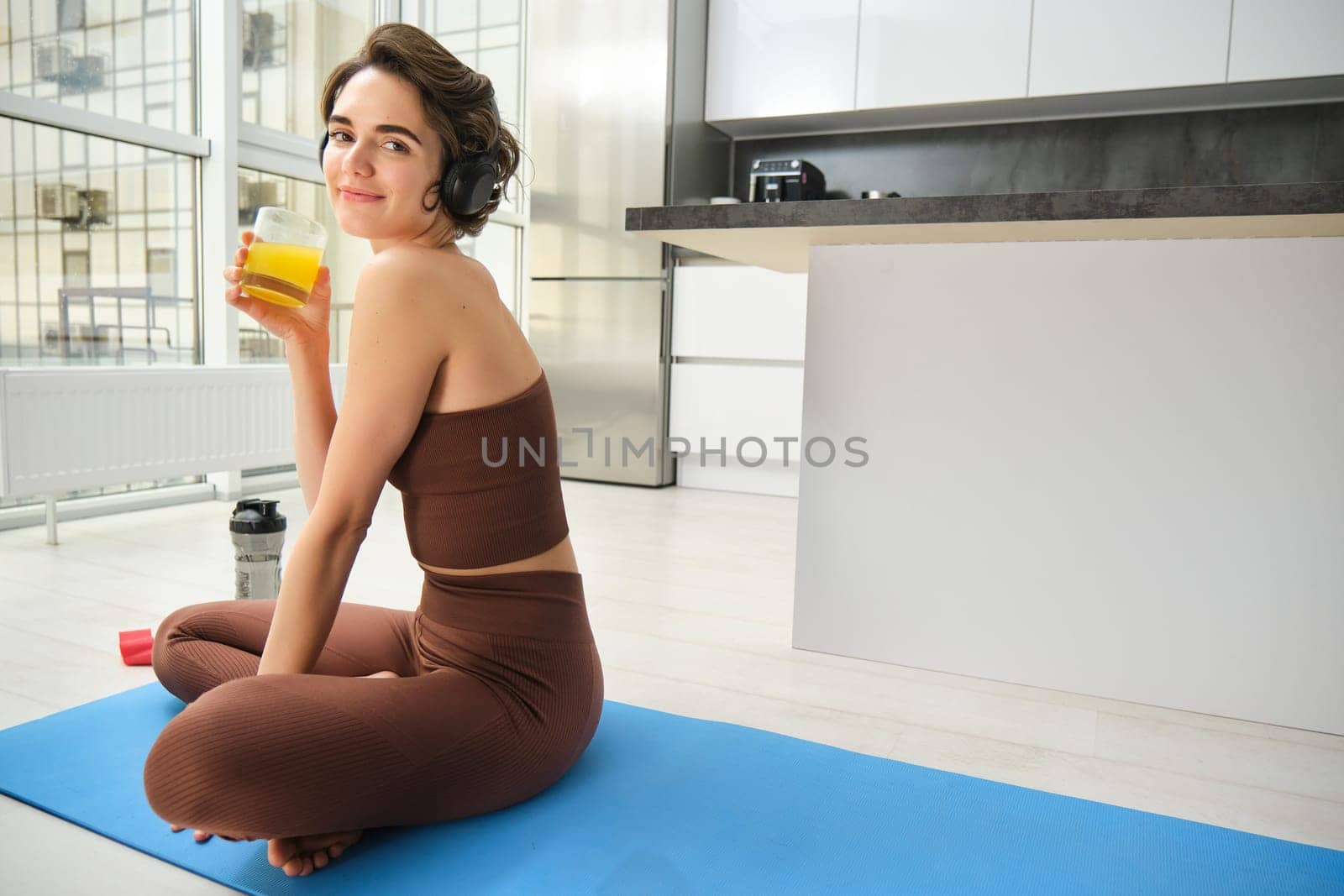 Sport and healthy lifestyle. Sportswoman at home, workout, drinks orange juice after fitness training, doing sports indoors on rubber mat.