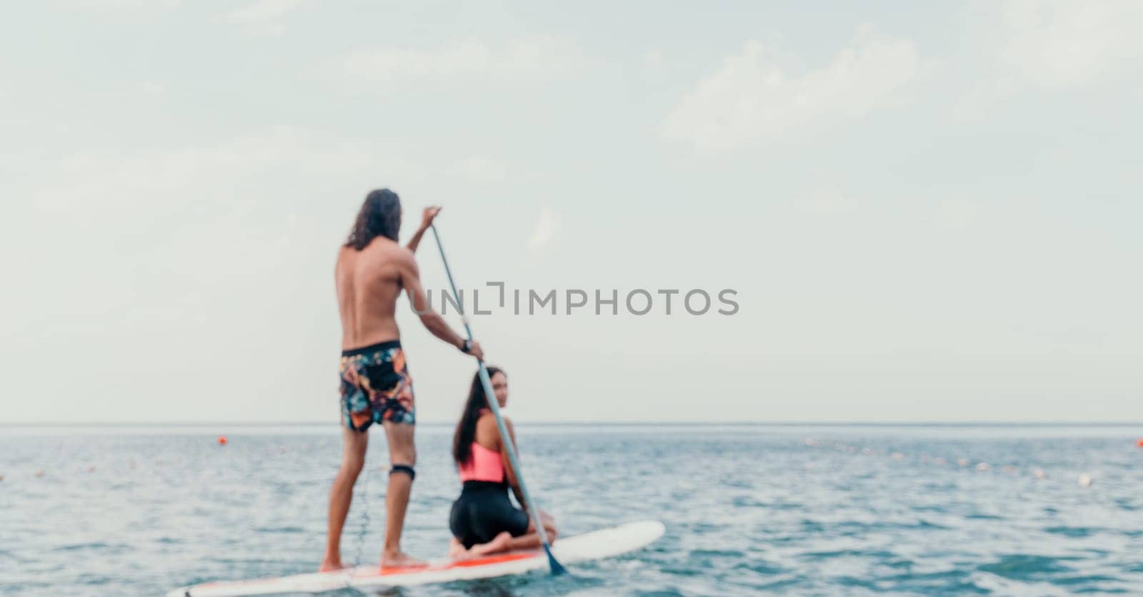 Sea woman and man on sup. Silhouette of happy young woman and man, surfing on SUP board, confident paddling through water surface. Idyllic sunset. Active lifestyle at sea or river