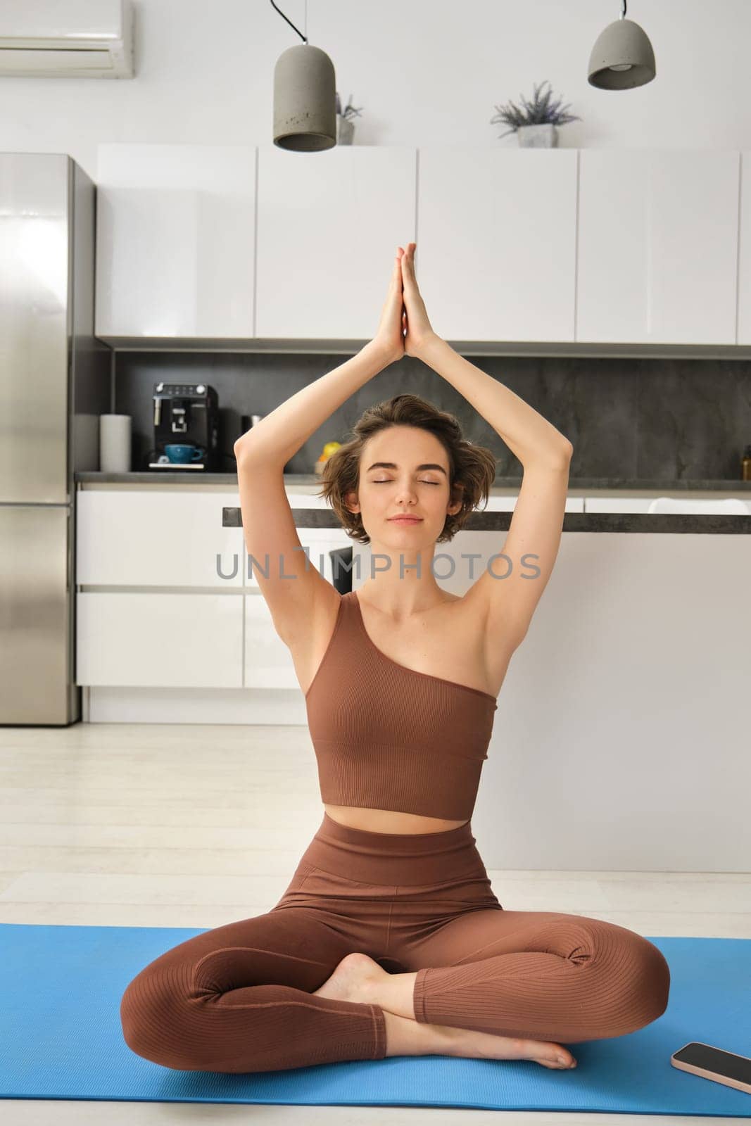 Portrait of fit and healthy woman in sportswear, doing yoga at home on fitness mat, making asana, relaxing and meditating indoors.