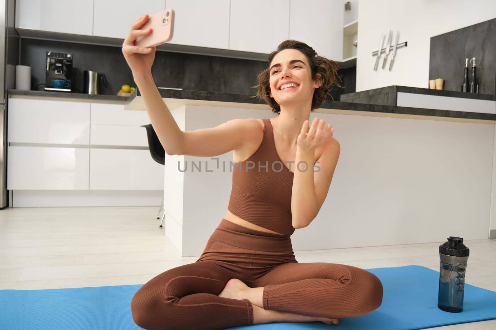 Lifestyle and workout. Modern fitness girl takes selfie on yoga mat, does her exercises at home and makes photos on smartphone, records live vlog, video on phone.