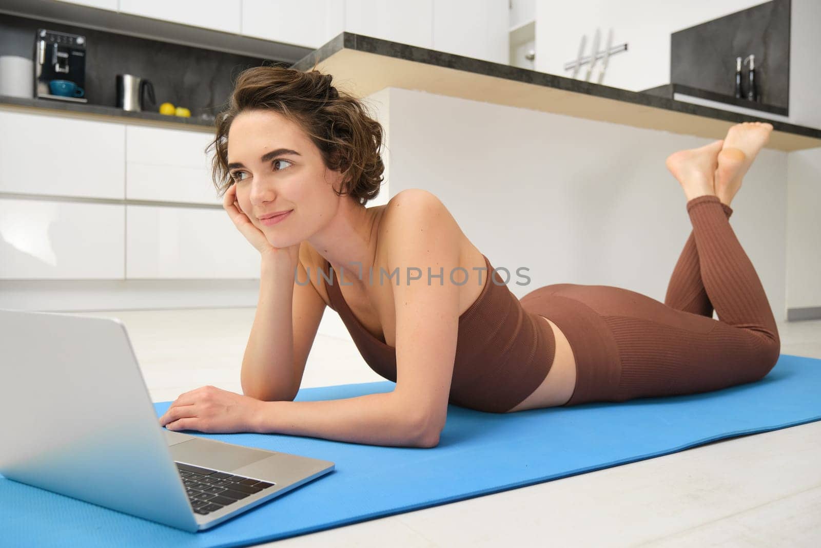 Portrait of woman athlete, girl workout at home, watches fitness videos on laptop, lying on rubber mat and doing indoor yoga session. Sport and wellbeing concept