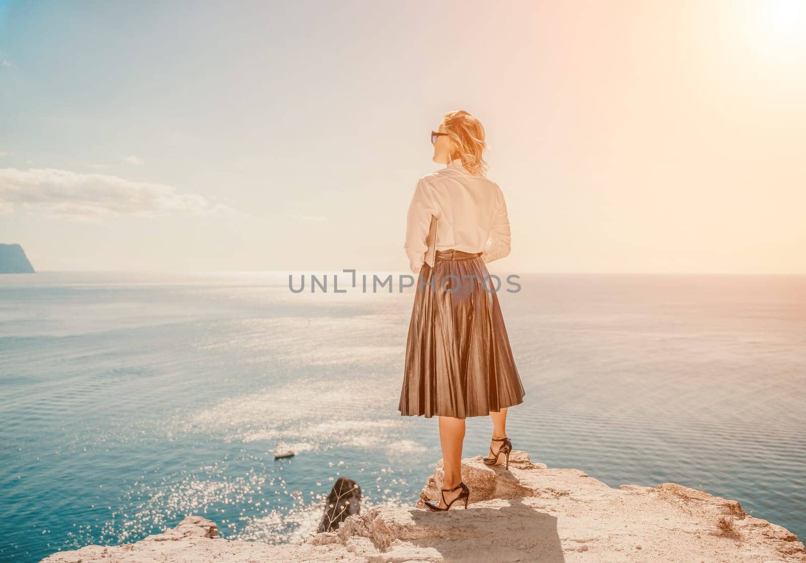 Business woman on nature in white shirt and black skirt. She works with an iPad in the open air with a beautiful view of the sea. The concept of remote work