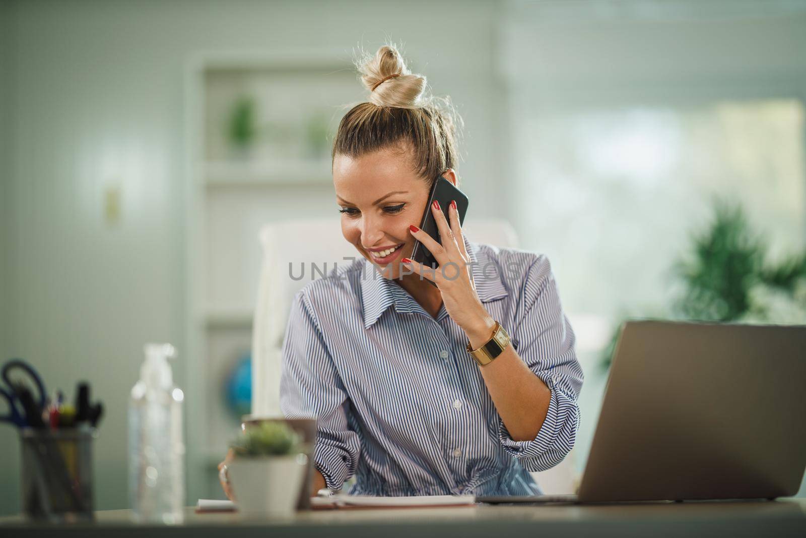 Shot of a attractive young woman using smartphone while working online on her laptop from home during COVID-19 pandemic.