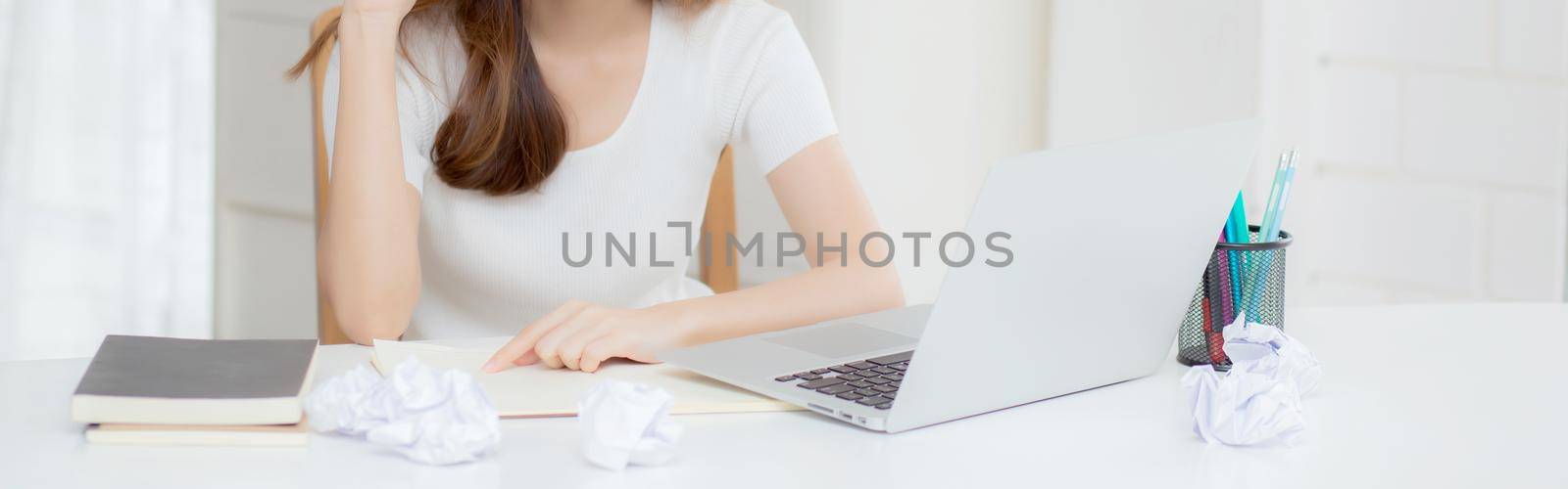 Young asian woman working with laptop computer think idea project and paper crumpled having problem on table at home, girl using notebook with frustrated and trouble, business and freelance concept.