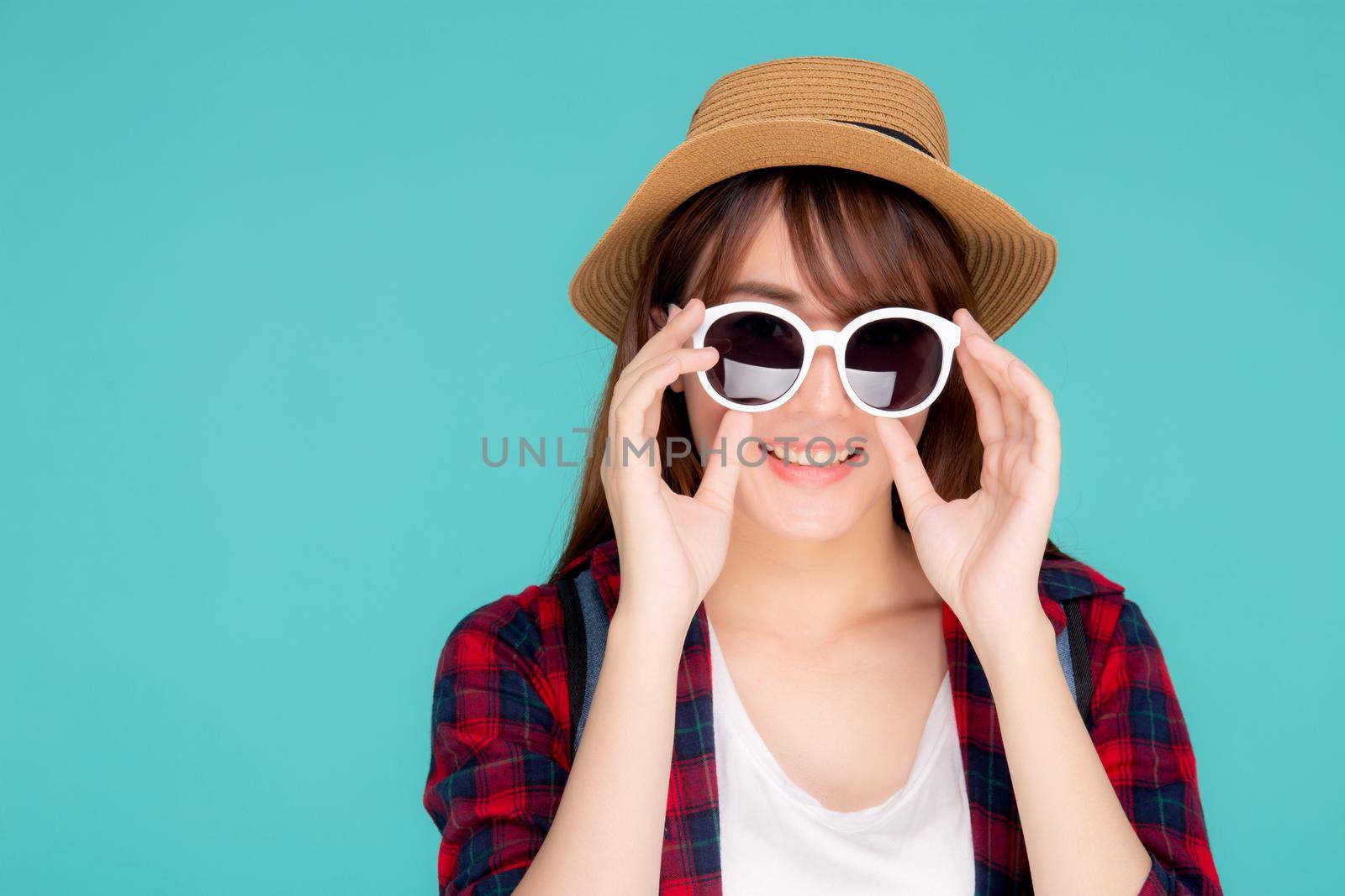 Beautiful portrait young asian woman wear hat and holding sunglasses smiling confident enjoy journey summer trip in vacation isolated on blue background, tourist asia girl cheerful with travel. by nnudoo