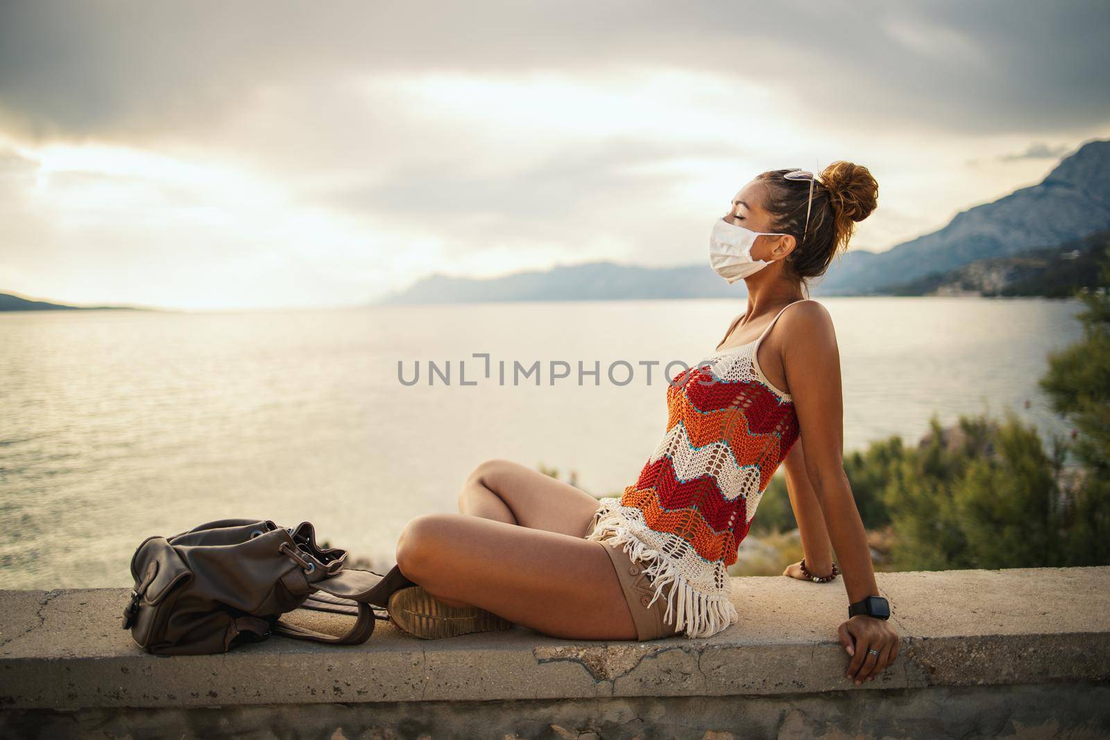 Shot of a happy young woman with protective mask spending time on seaside during exploring a Mediterranean at corona pandemic. 