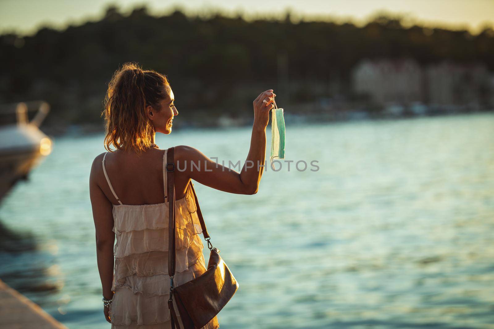 Shot of an attractive young woman with surgical mask enjoying a vacation at seaside during the COVID-19.