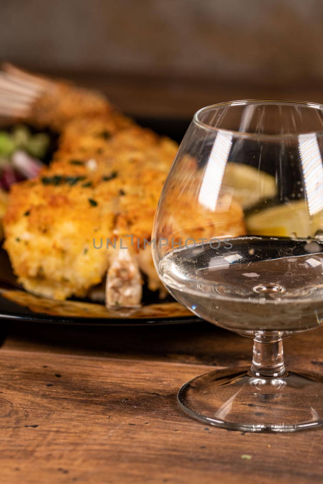glass of white wine with fish plate behind on wooden 
