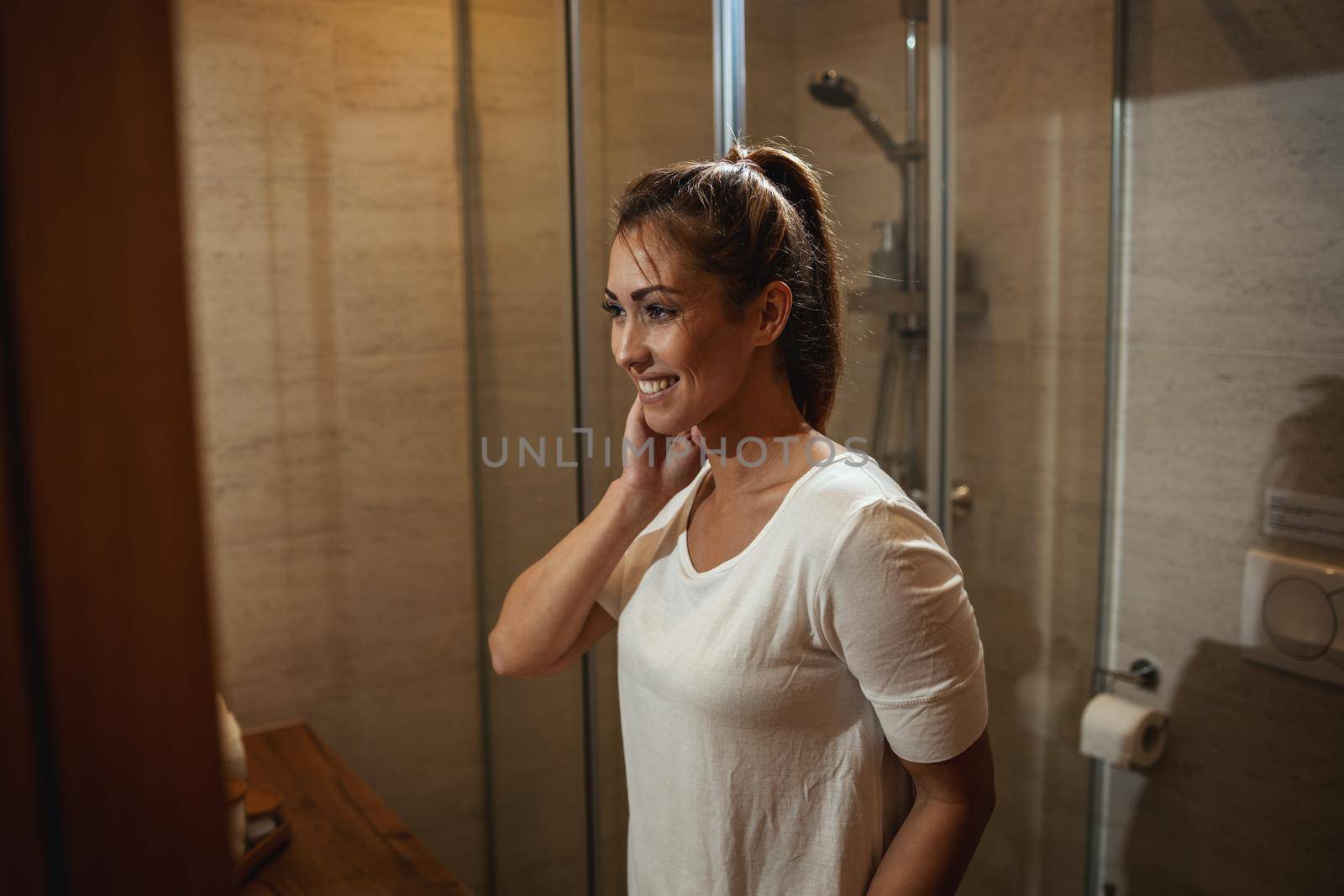 Attractive young woman admiring her face while standing in front of the bathroom mirror at home.