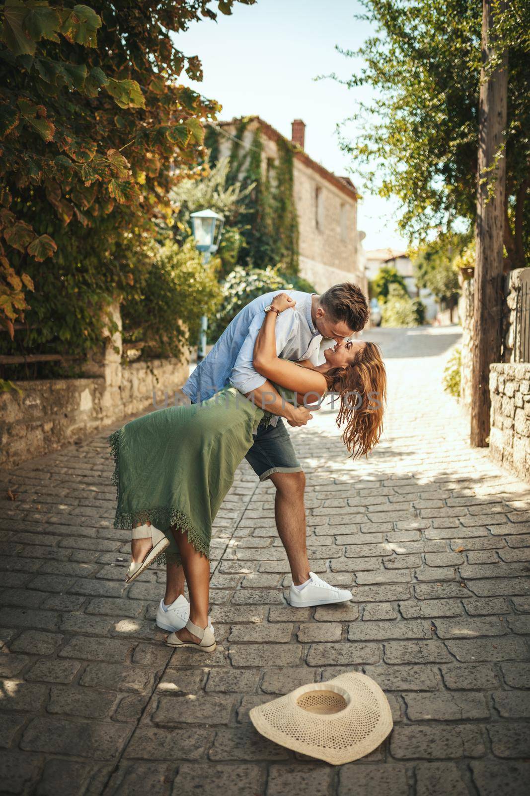 A beautiful young couple is having fun and dancing on the street while walking along of a Mediterranean town. They are enjoyed in summer sunny day.
