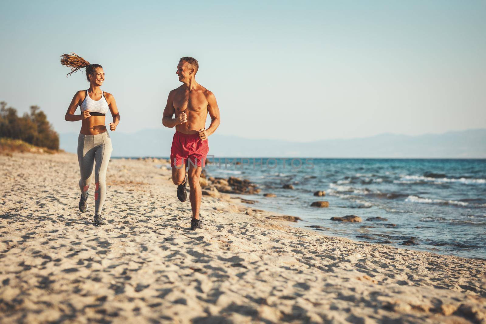 A smiling happy couple is running along the sea shore and enjoying in summer sunny day.