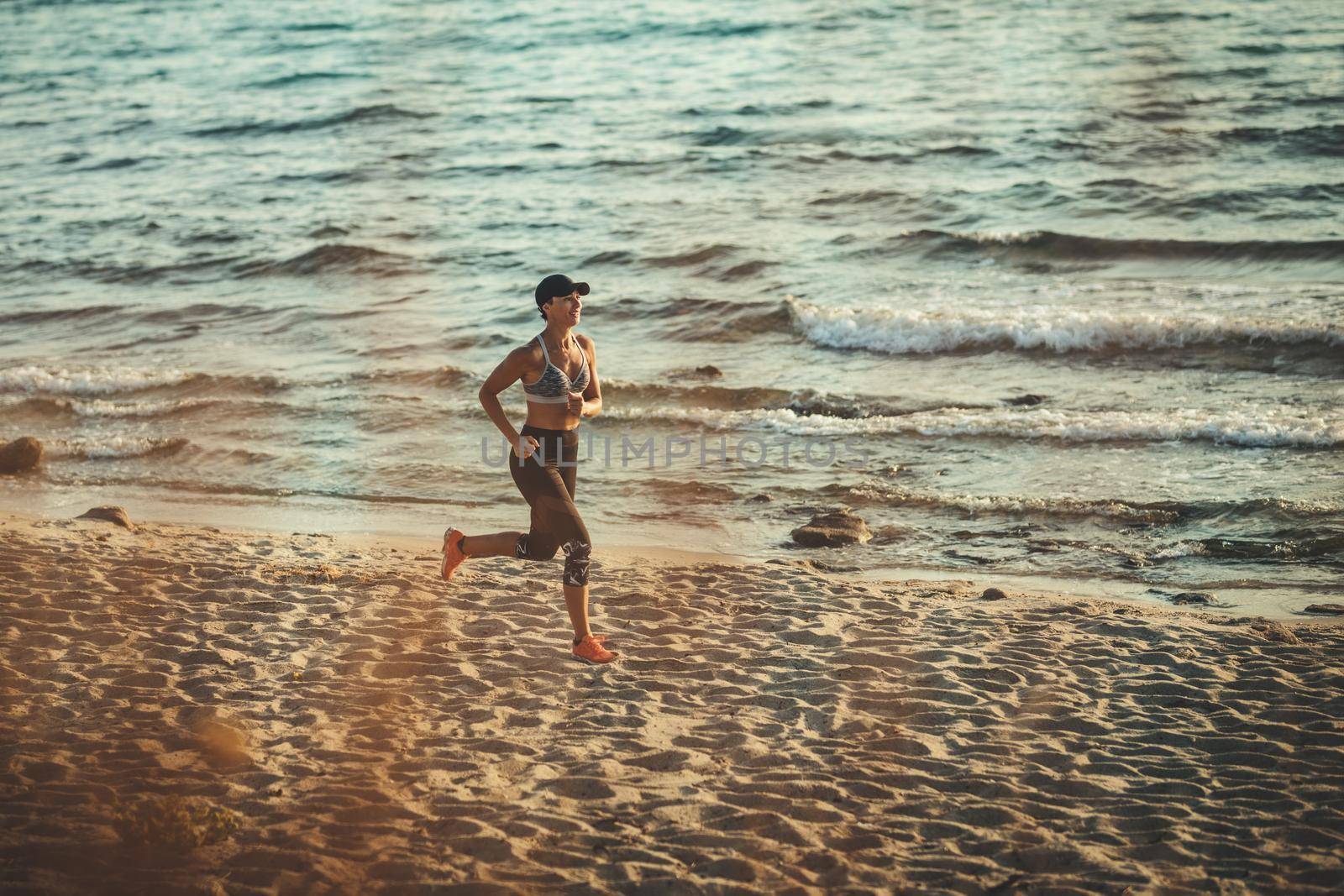 Young woman is running along the sea shore on the beach during the hot summer vacation day.