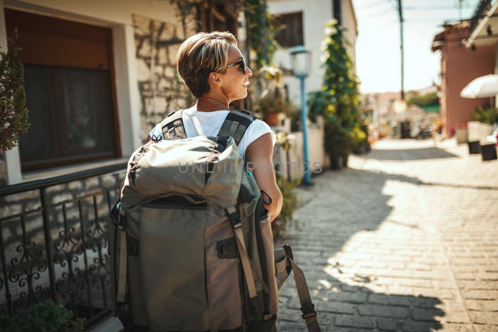 A beautiful young tourist arrived in a Mediterranean city with a backpack on her back. She is enjoying in summer sunny day.