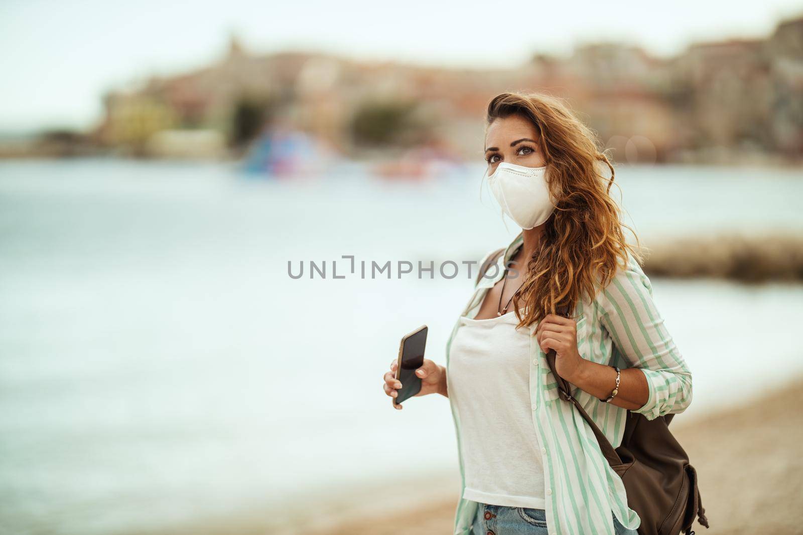 Shot of an attractive young woman with protective N95 mask enjoying a vacation on the beach during the COVID-19.