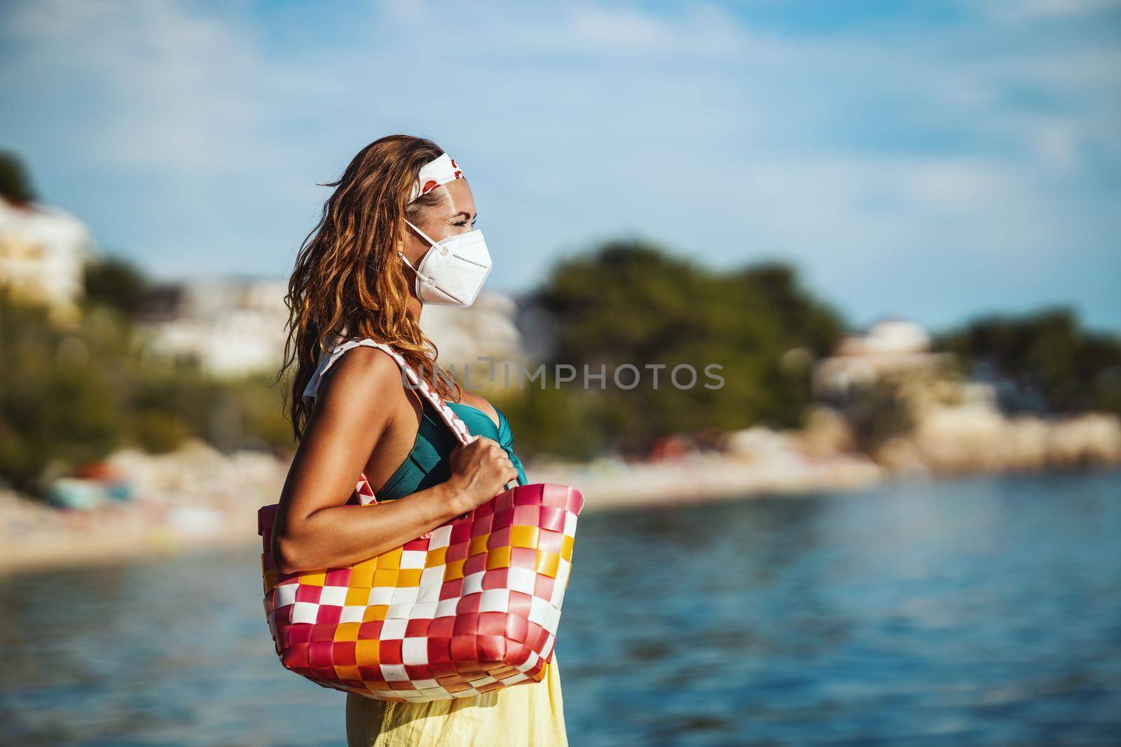 Shot of an attractive young woman in bikini with surgical mask enjoying a vacation on the beach during the COVID-19.