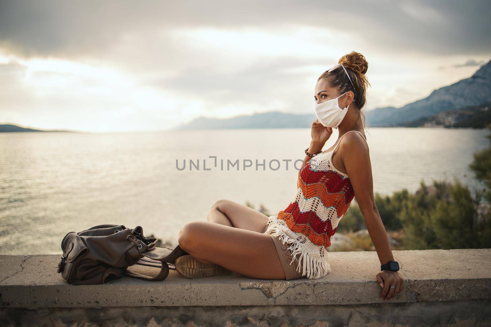 Shot of a happy young woman with protective mask spending time on seaside during exploring a Mediterranean at corona pandemic. 