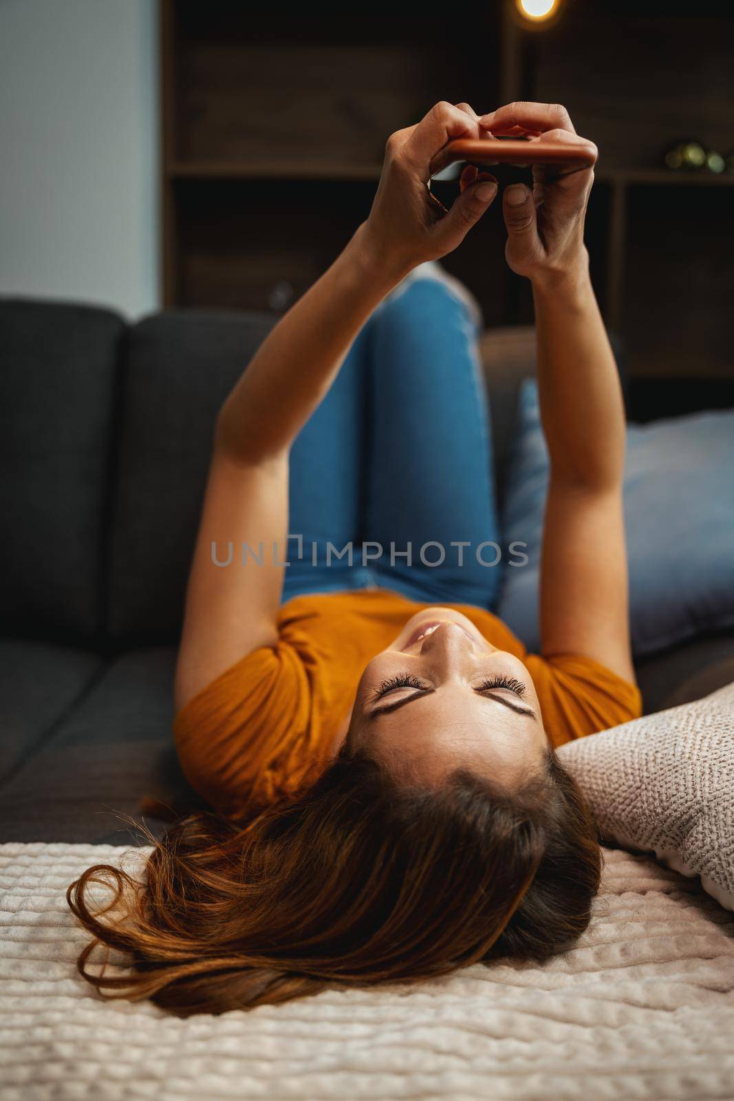 Attractive young woman lying on the sofa and using smartphone to surfing social media at home.