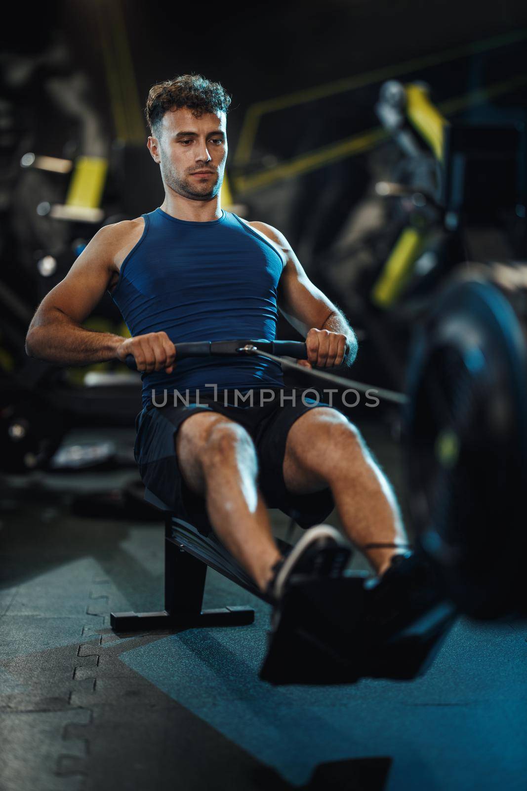 A young muscular man is pulling the row machine on crossfit training in the gym.
