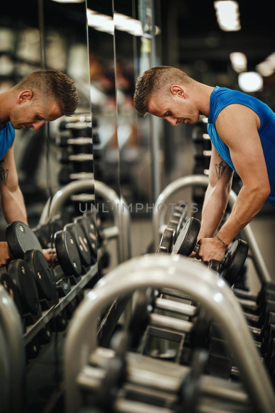 Shot of a muscular guy in sportswear working out at the hard training in the gym. He is pumping up muscule with heavy weight.
